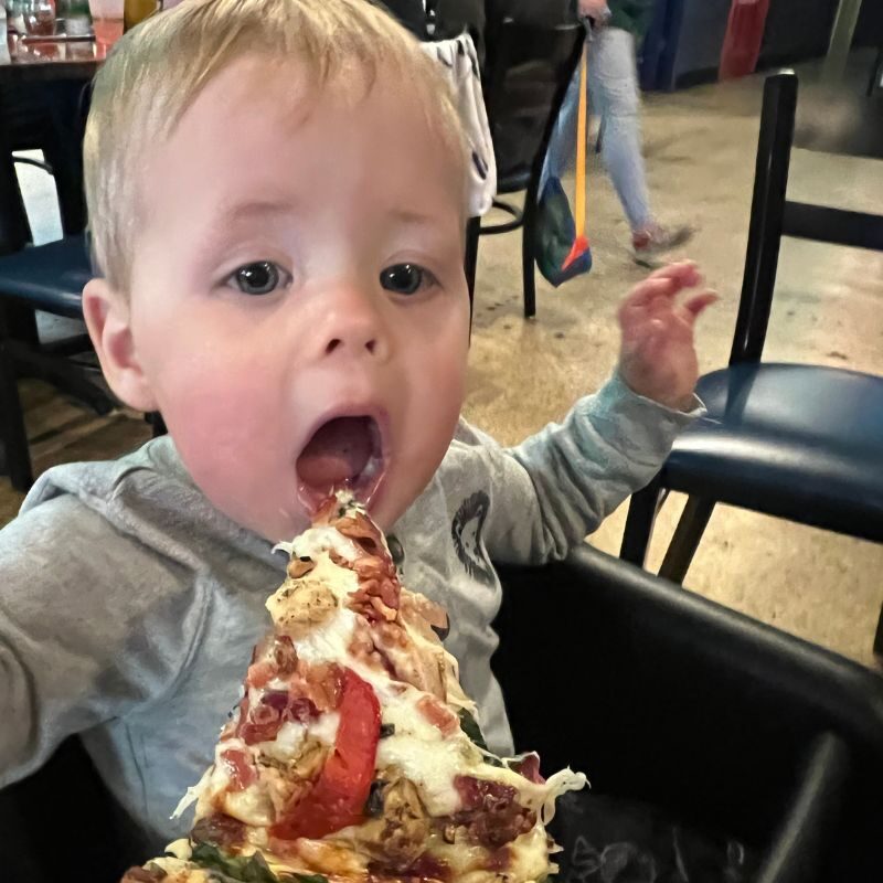 A toddler devours a piece of pizza. 