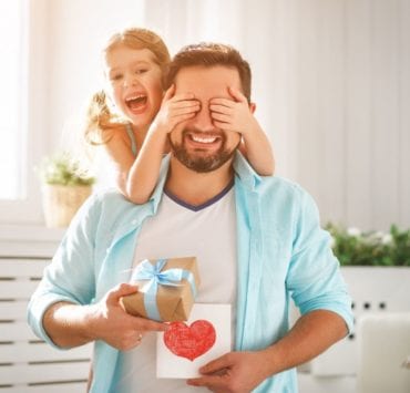 little girl covering her das's eyes while he holds a gift