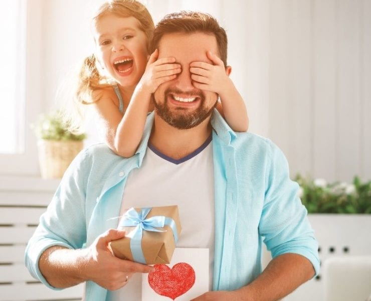little girl covering her das's eyes while he holds a gift