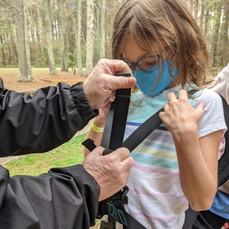 A young girl has her harness properly checked for safety during her visit to Raptor Aerial Adventure Park.