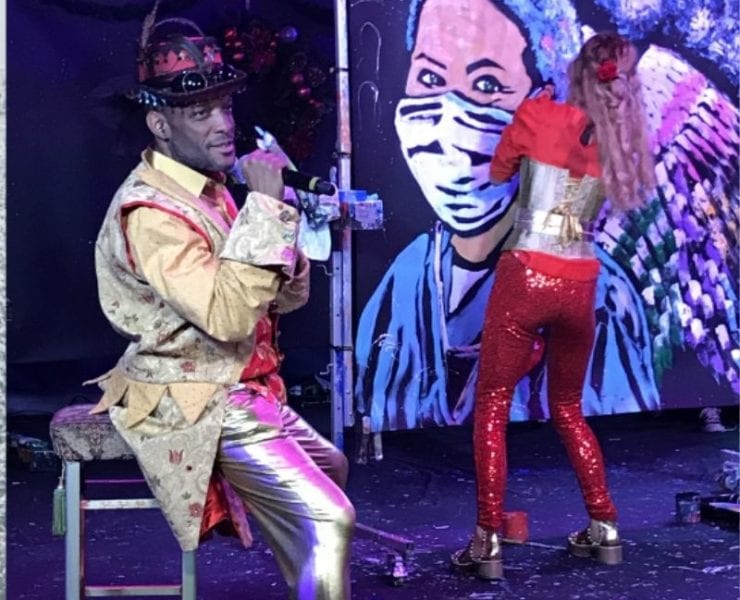 a man sitting on a stage at the ArtRageous show painting a portrait of a nurse wearing a face mask