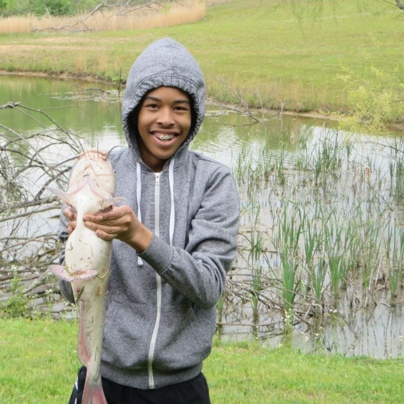 boy holding up a fish at a pond