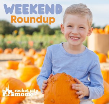 A boy in a blue shirt holds a warty orange pumpkin in front of a pumpkin patch.