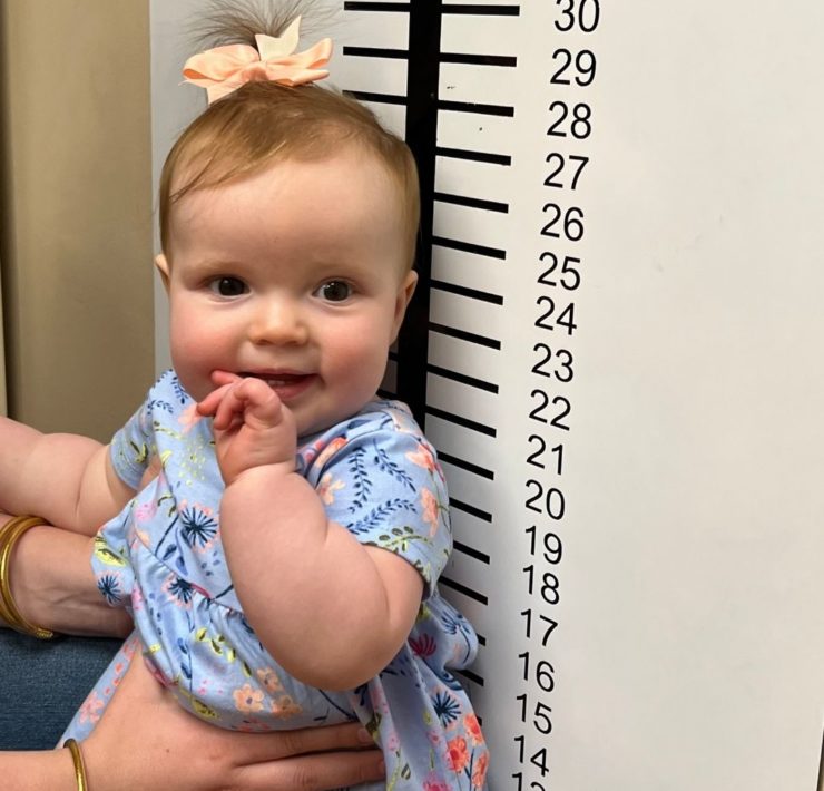A baby girl leans against a measuring chart on the wall of the doctor's office at the Imagination Place.