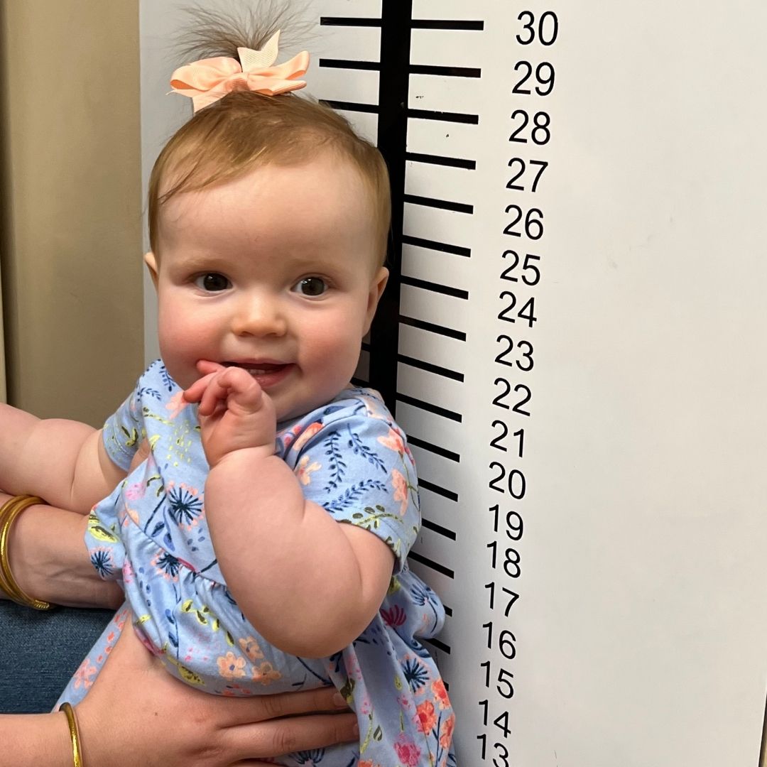 A baby girl leans against a measuring chart on the wall of the doctor's office at the Imagination Place.