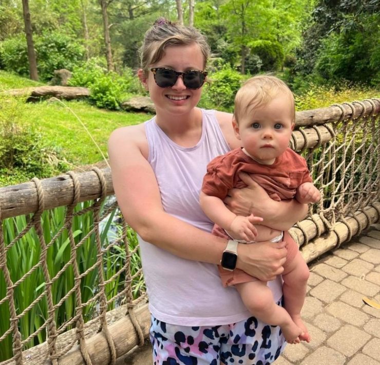 A woman in purple stands in front of the gibbons habitat with her baby at the Nashville Zoo.