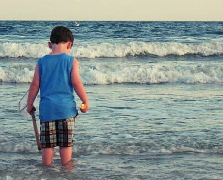 little boy standing in the water at the beach