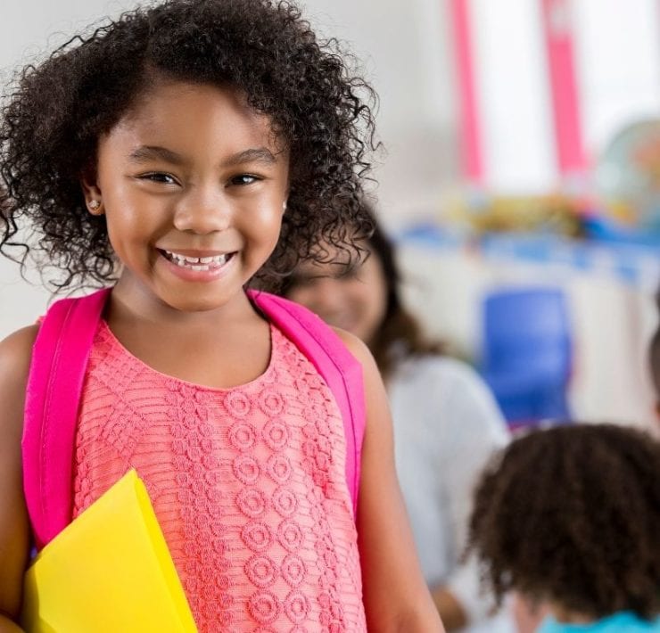 young girl in school classroom with backpack