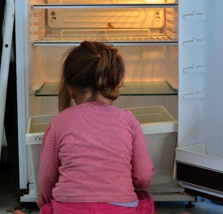 hungry child sitting in fron tof empty refrigerator