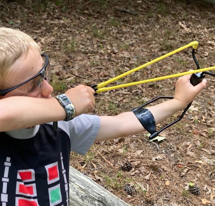 A young boy takes aim with a yellow slingshot at PIne Ridge.