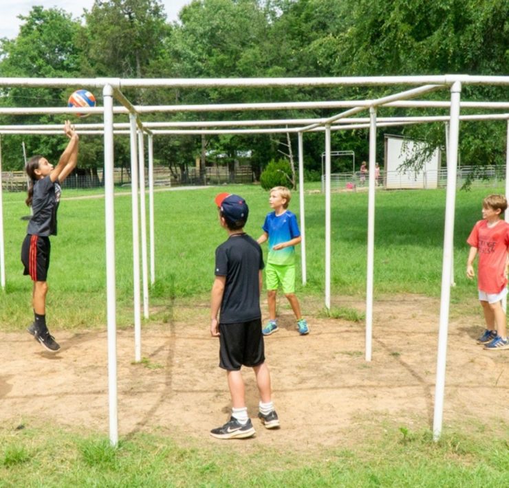 A young boy dangles just above the ground as he completes an obstacle course with his friends cheering him on.