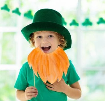 A young boy holds a paper beard and wears green as part of Saint Patrick's Day.