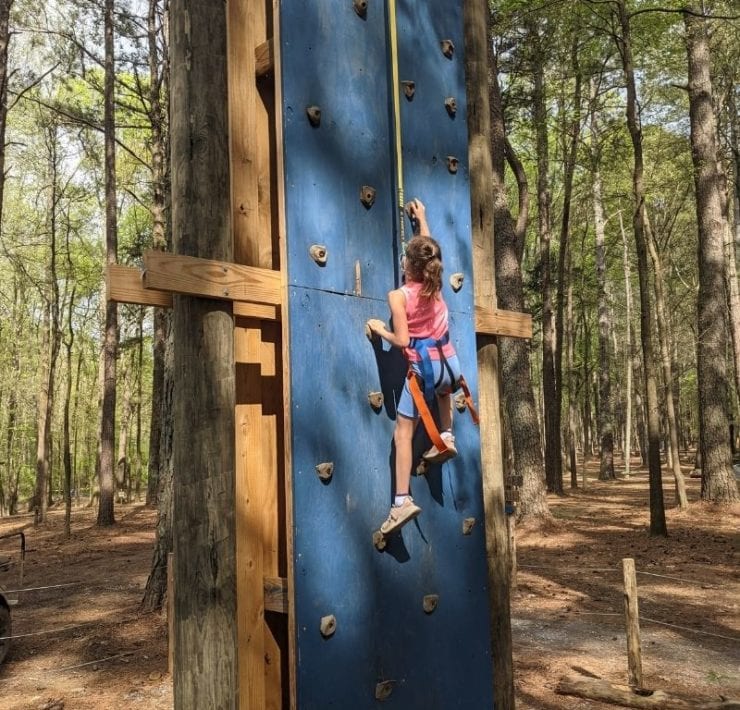 A girl climbs towards the top of a rock climbing wall at GoFAR USA Park.