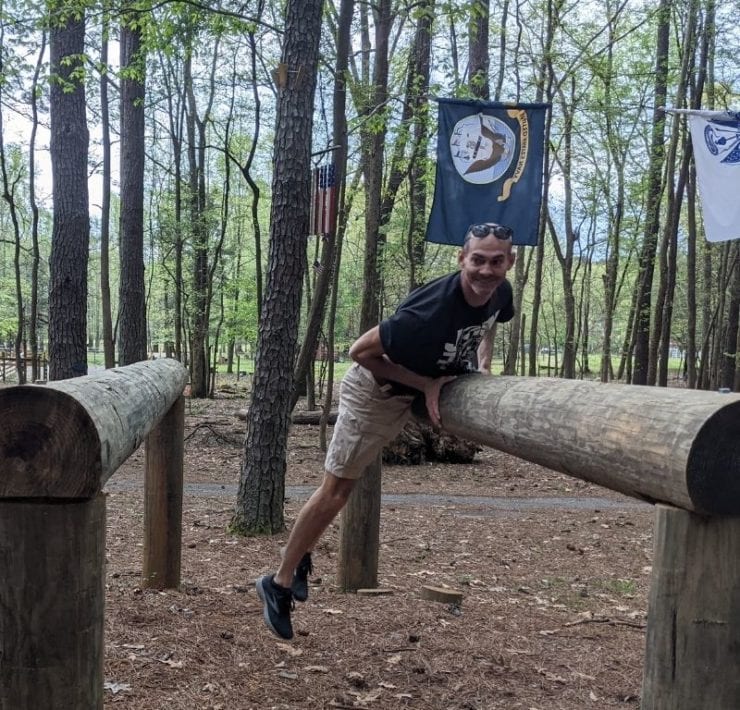 A man climbs over a log hurtle at the obstacle course section of GoFAR USA.