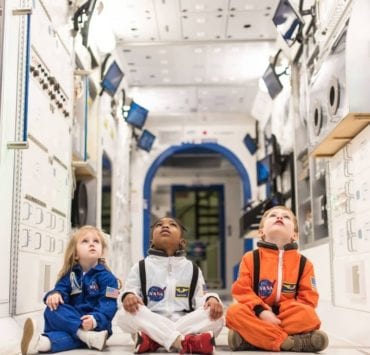 three young children in astronaut suits sitting in a space shuttle