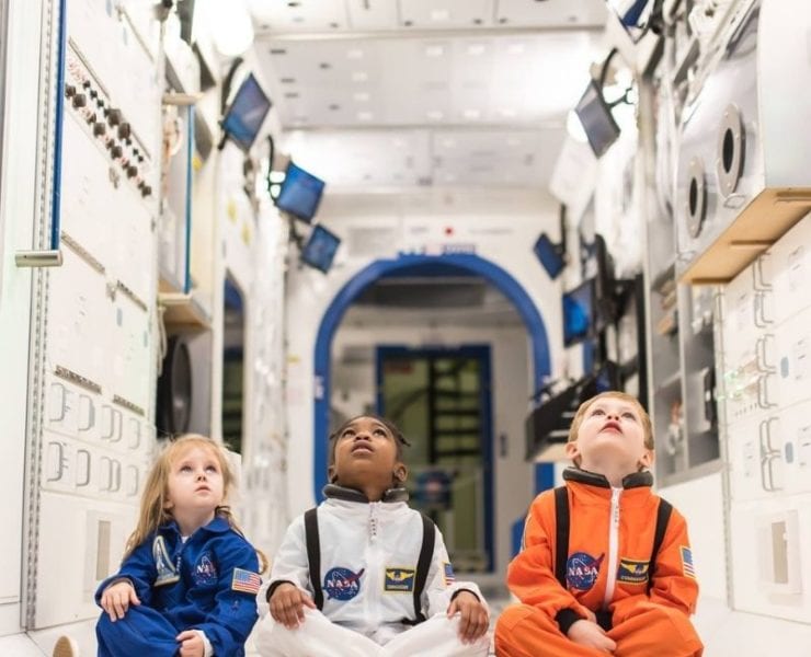 three young children in astronaut suits sitting in a space shuttle