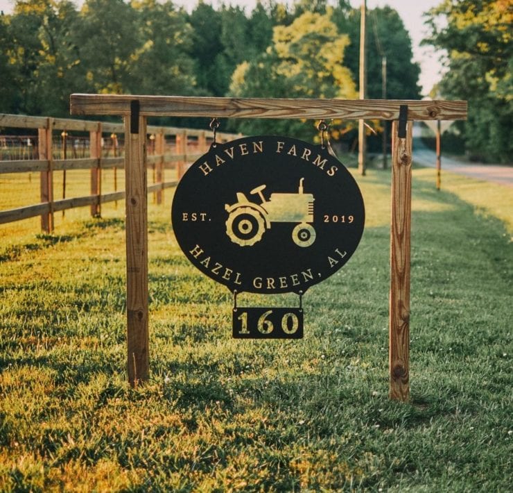 A black metal sign with a tractor in the center hangs at the entrance of Haven Farms.