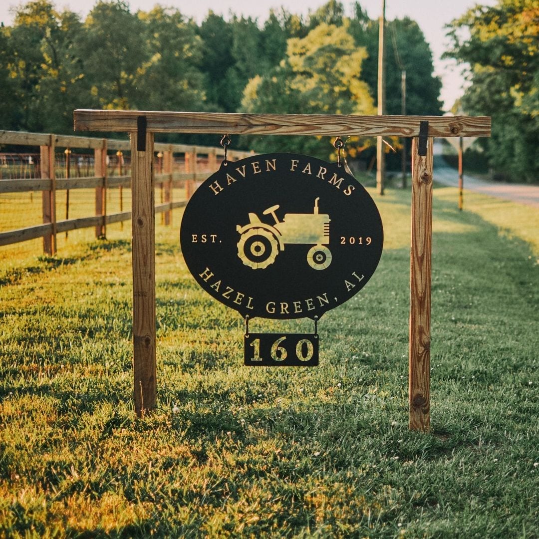 A black metal sign with a tractor in the center hangs at the entrance of Haven Farms.