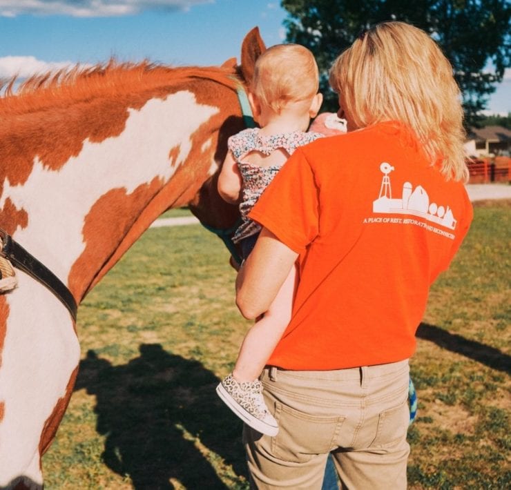 LeAnn Newsom holds a toddler as she introduces her to one of the resident horses on Haven Farm.