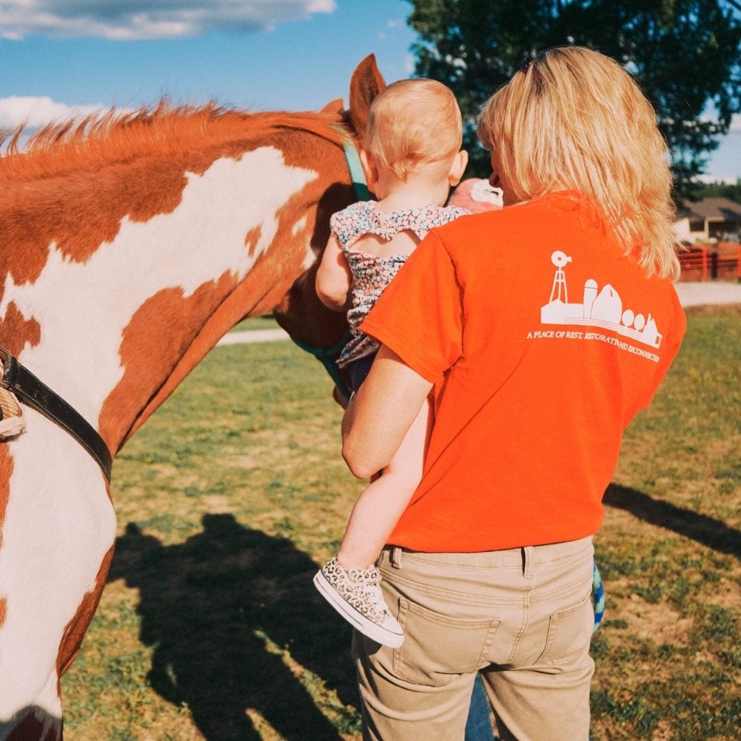 LeAnn Newsom holds a toddler as she introduces her to one of the resident horses on Haven Farm.