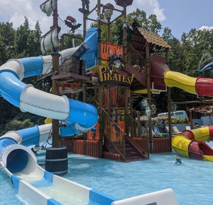 A blue and white slide and a red and yellow slide are part of a pirate ship shaped play area.