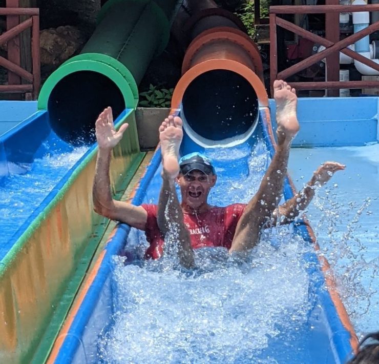 A man makes a splash as he comes out of the end of an orange slide.