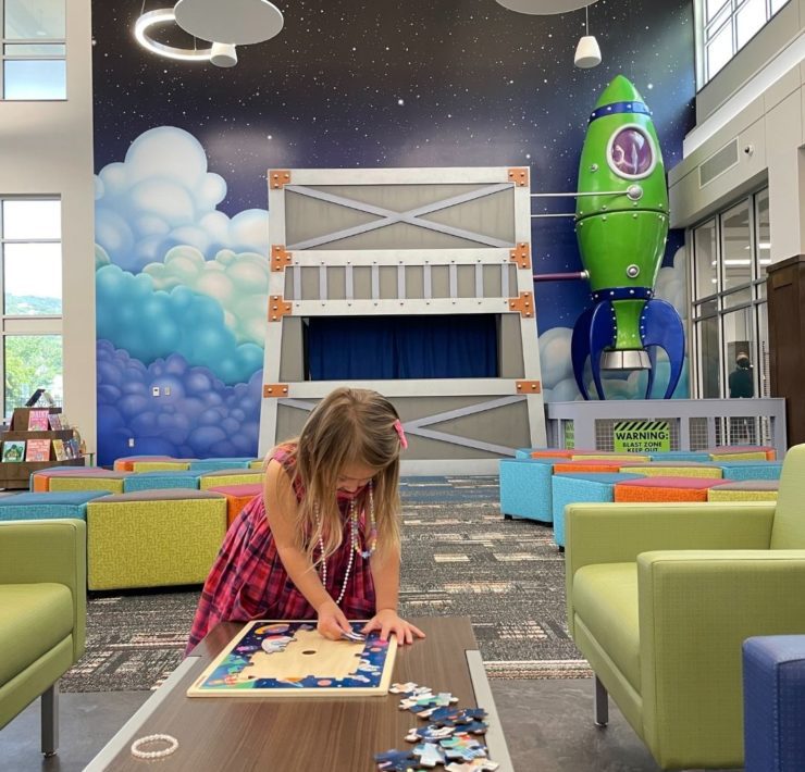 A girl completes a puzzle in front of the galactic mural at the children's area of the South Huntsville Library.