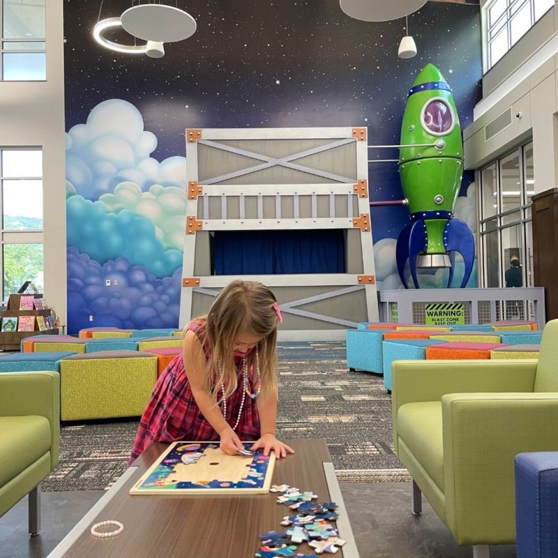 A girl completes a puzzle in front of the galactic mural at the children's area of the South Huntsville Library.