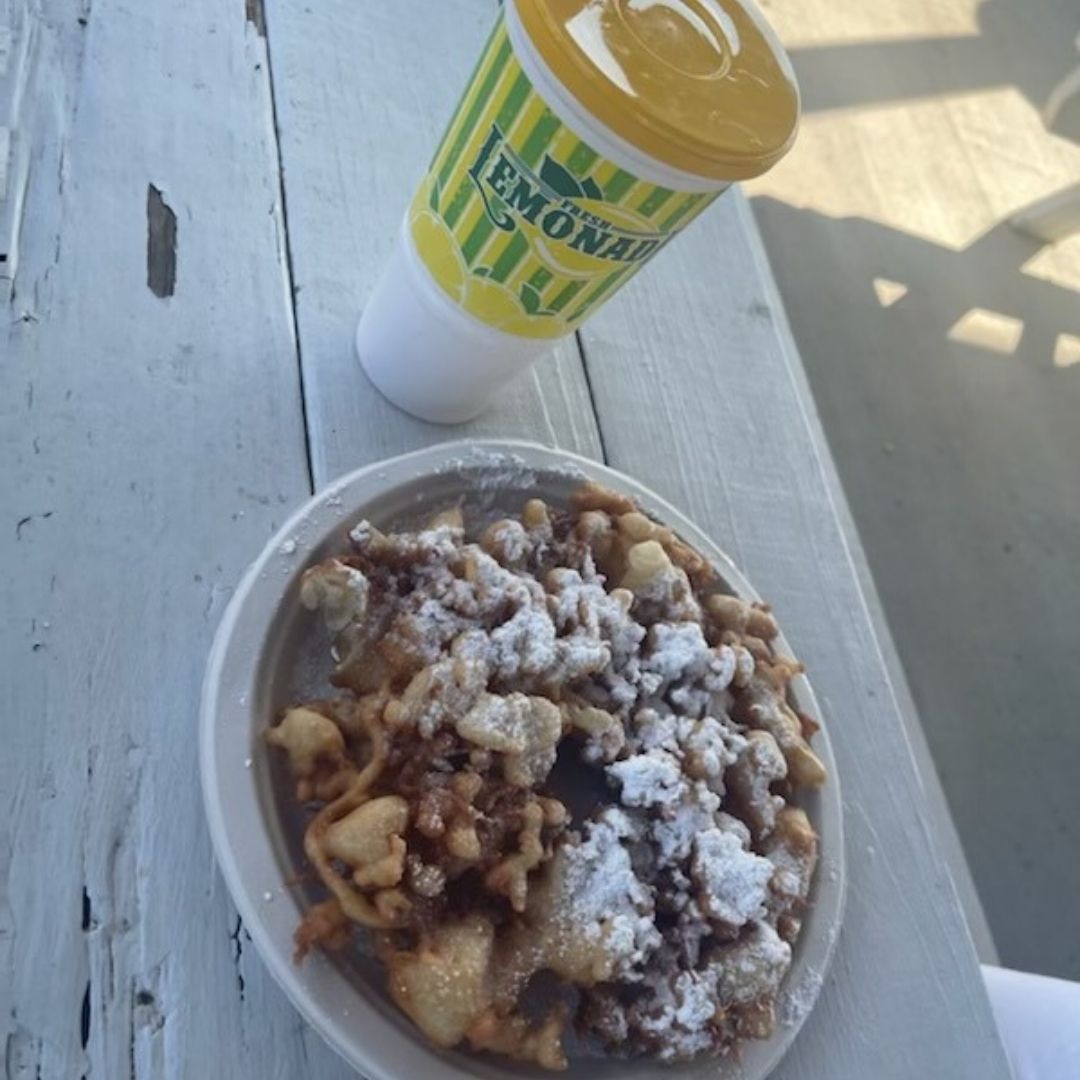 A cup of lemonade and a plate of funnel cake sits on a wooden table at the farm.