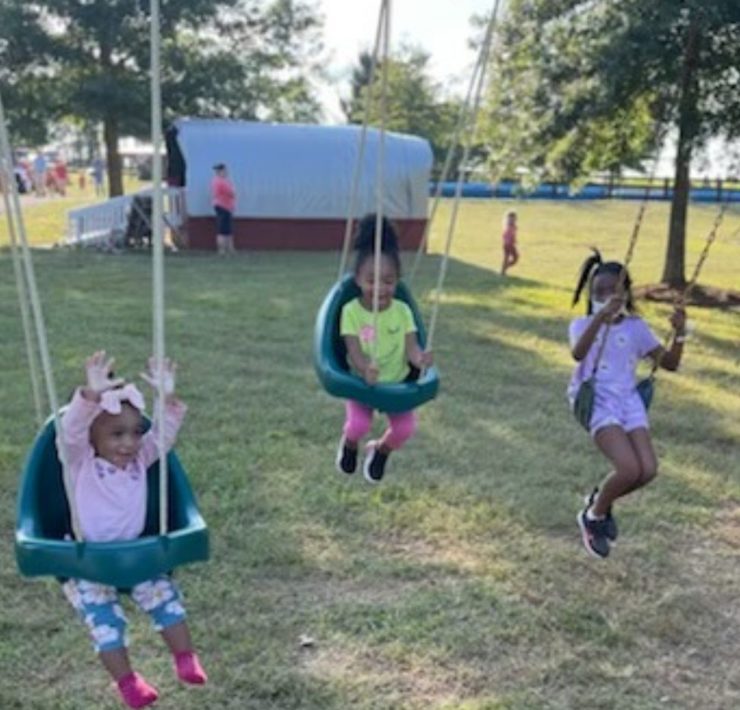 Three girls swing at the play area on the farm.