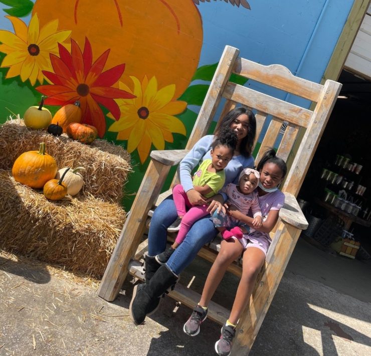 A family sits in an oversized wooden chair outside Lyon Family Farm.
