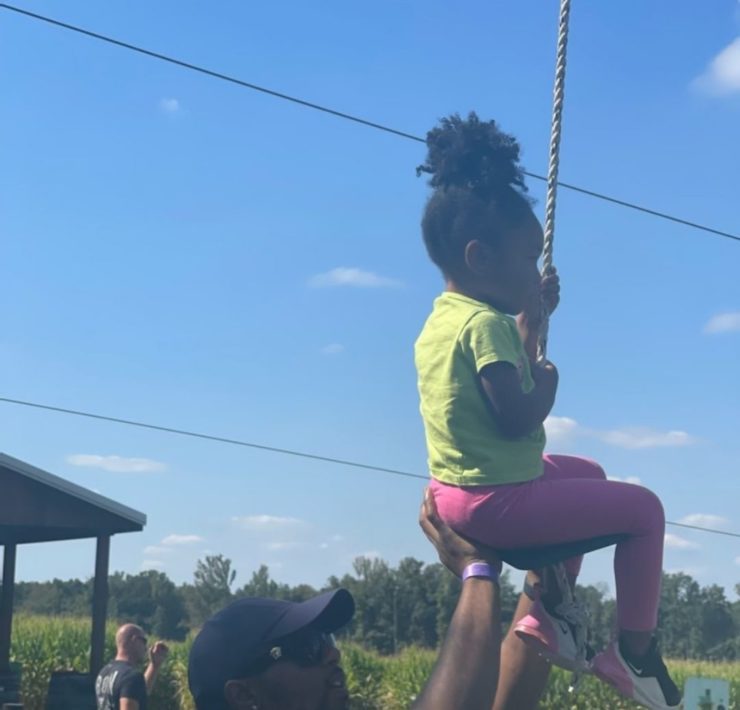 A young girl ziplines with the help of her dad.