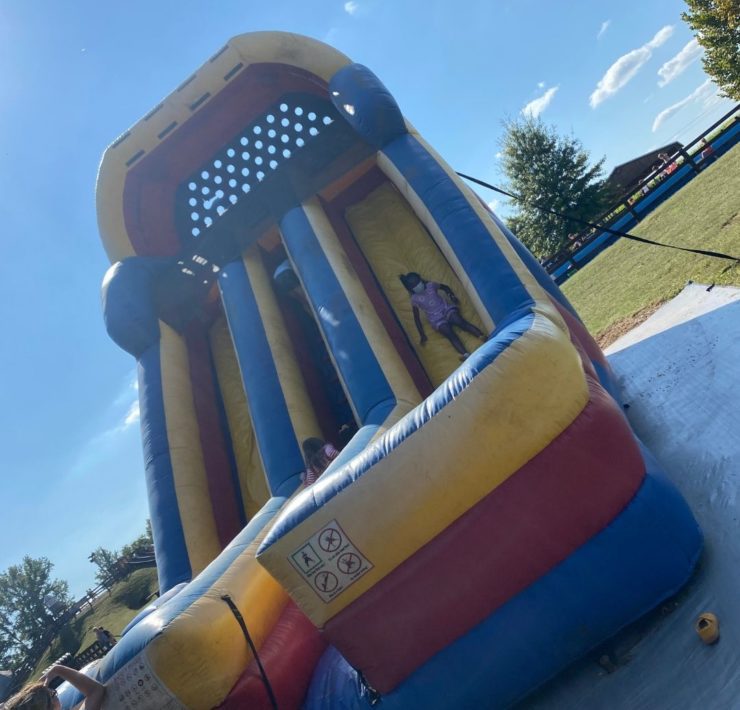 A girl slides down a large yellow, red, and blue inflatable slide.