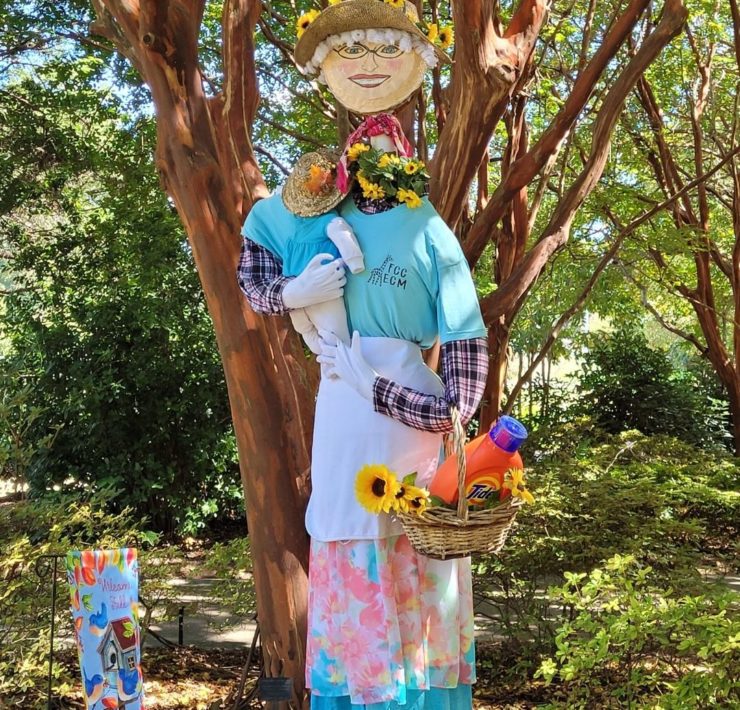 A scarecrow features a baby scarecrow and a basket of laundry materials in the Huntsville Botanical Garden.