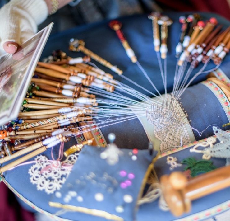 A small thing of lace is being intricately woven over blue upholstery.