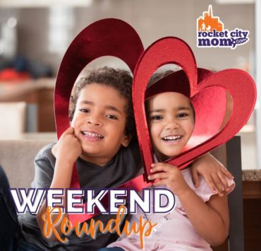 Two young children hold red paper hearts as part of their Valentine's Day fun during their Huntsville Weekend.