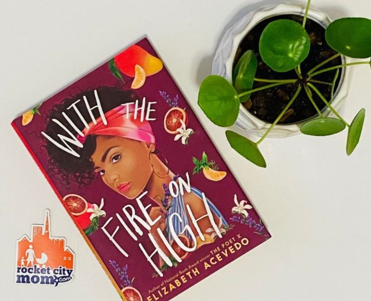 The book "With the Fire on High" sits on a white table next to a green plant and orange and purple Rocket City Mom sticker.