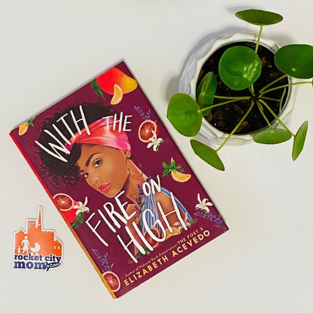 The book "With the Fire on High" sits on a white table next to a green plant and orange and purple Rocket City Mom sticker.