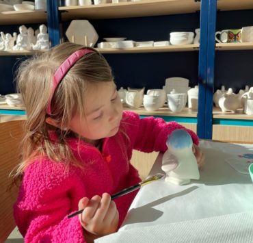 A young girl in pink paints a ceramic penguin at Color Me Mine.