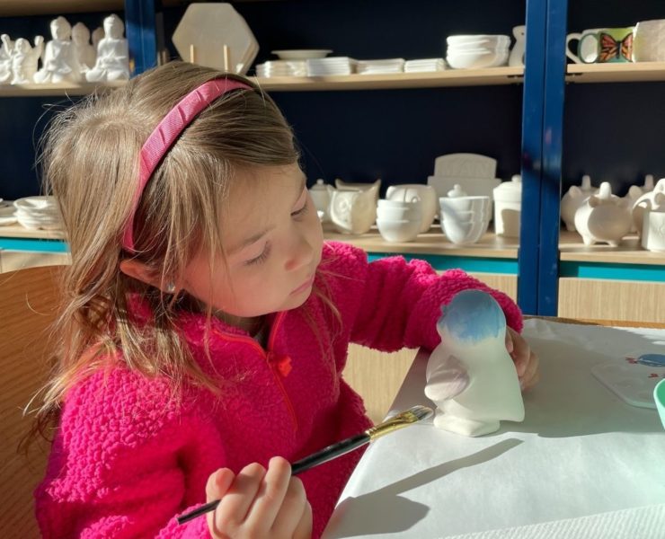 A young girl in pink paints a ceramic penguin at Color Me Mine.
