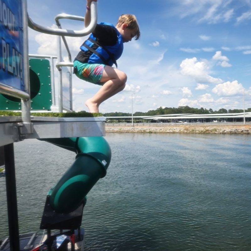 A young boy in a blue life jacket jumps from the a platform into the water.