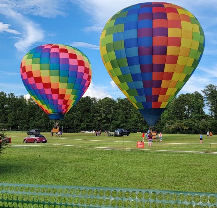 Two rainbow colored hot air balloons are tethered in a large green field at Callaway Gardens.
