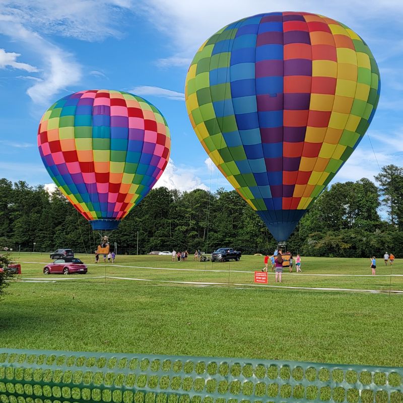 Two rainbow colored hot air balloons are tethered in a large green field at Callaway Gardens.