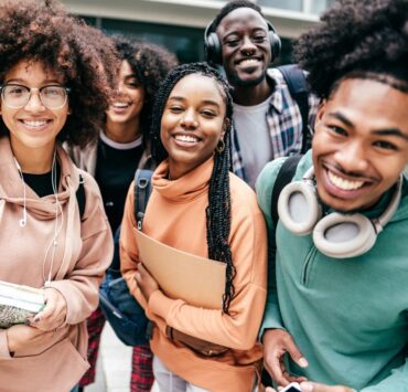 A group of teens hold books and notebooks in preparation of college applications.
