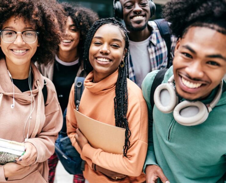 A group of teens hold books and notebooks in preparation of college applications.