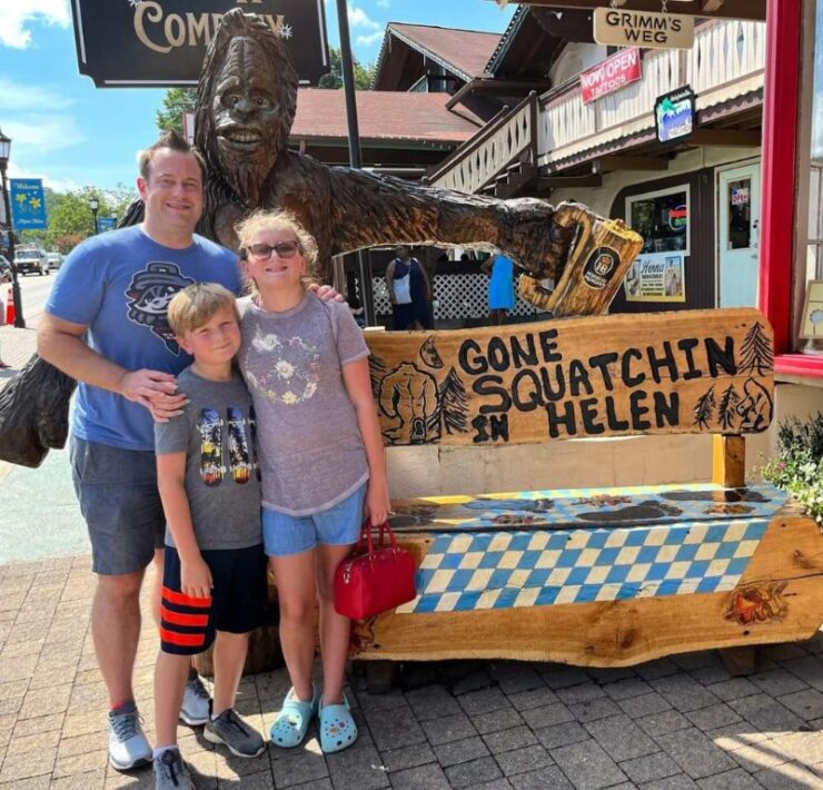 A dad and his daughter and son stand in front of a sasquatch sign in Helen, GA.