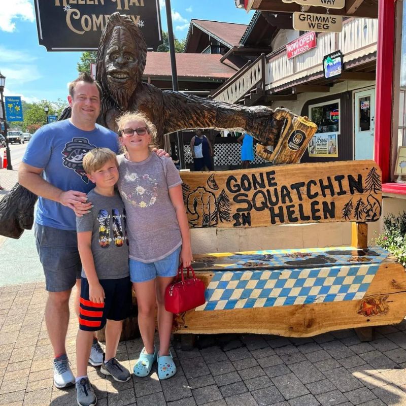 A dad and his daughter and son stand in front of a sasquatch sign in Helen, GA. 