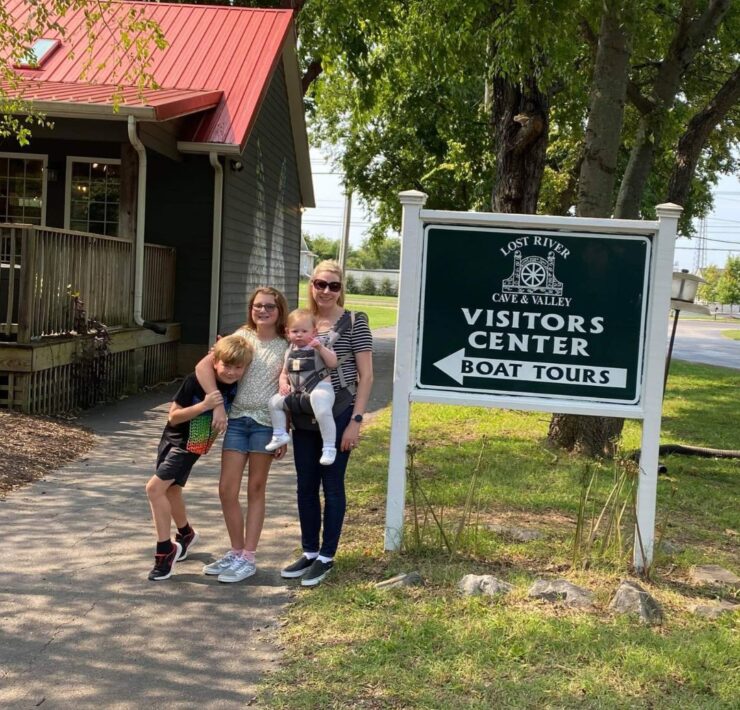 A mother and three children stand beside a visitor's center sign for Lost Rivers Cave in Bowling Green, KY.