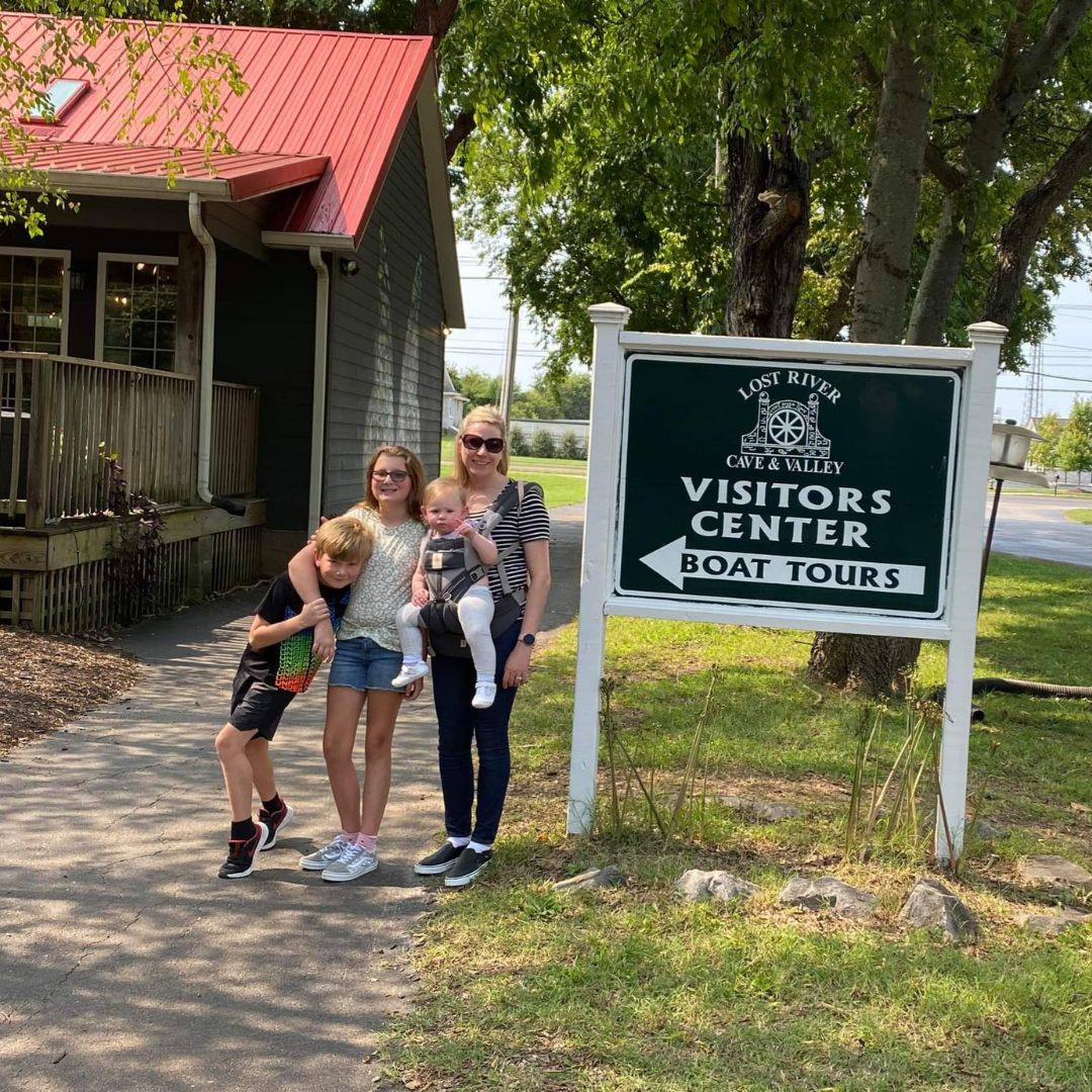 A mother and three children stand beside a visitor's center sign for Lost Rivers Cave in Bowling Green, KY.