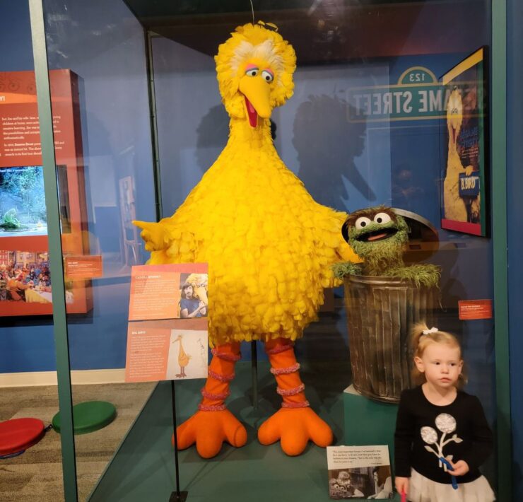 A young girl stands next to a display of Sesame Street's Big Big and Oscar the Grouch at the Center for Puppetry Arts.